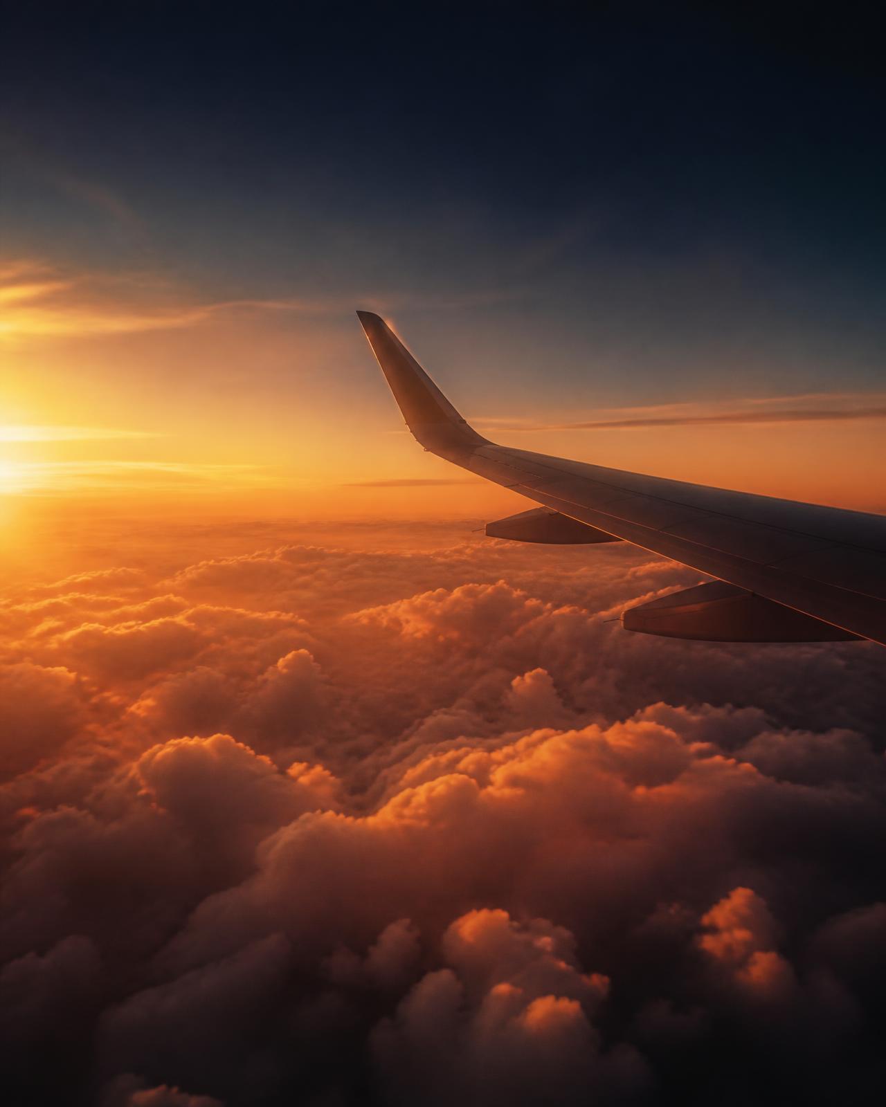 Airplane wing above the clouds at sunset